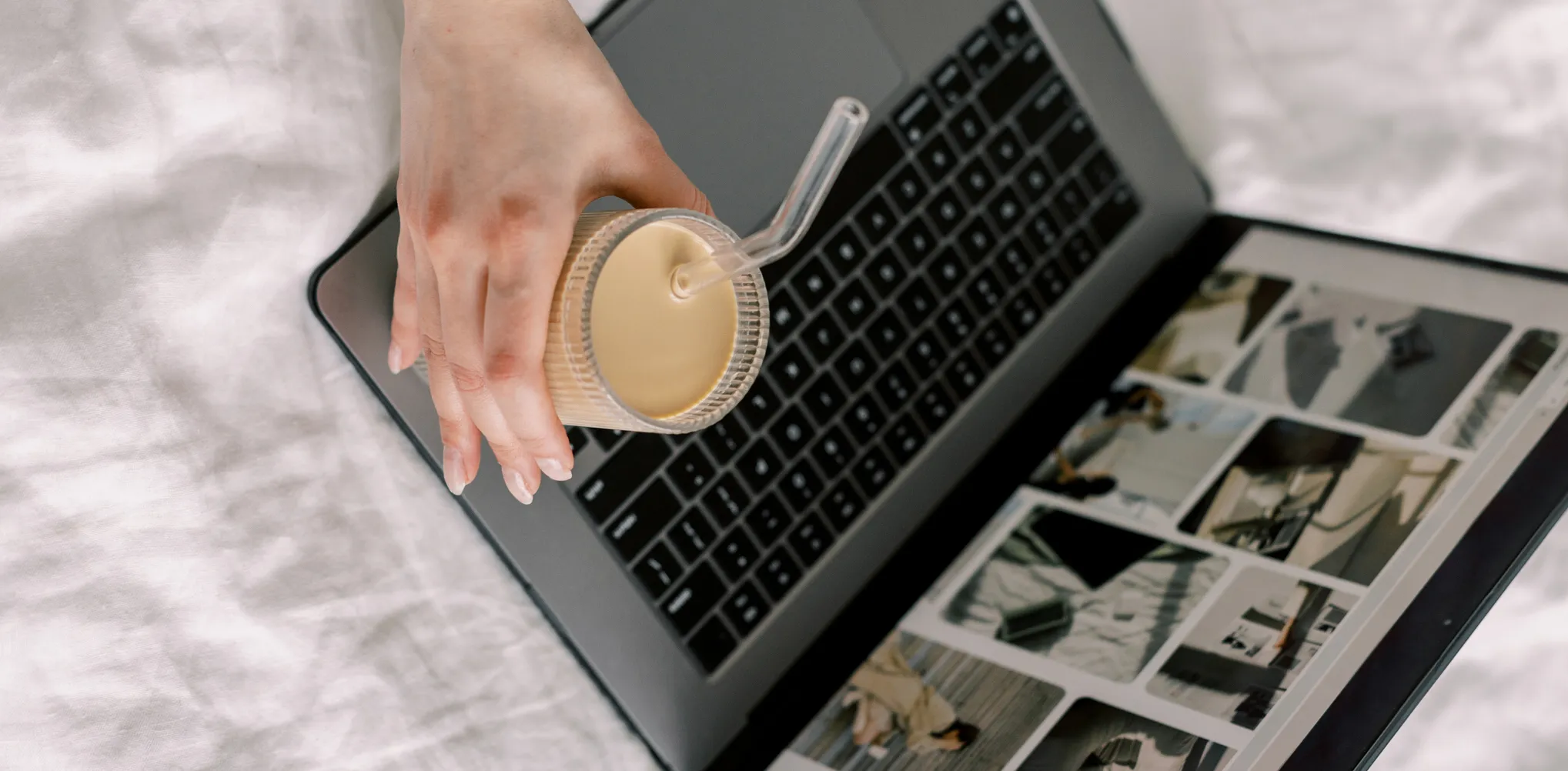 Woman holding a glass of iced coffee and a laptop in front of her with images on the screen.